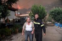 A firefighter helps a local as a wildfire burns at the village of Kontodespoti, on the island of Evia