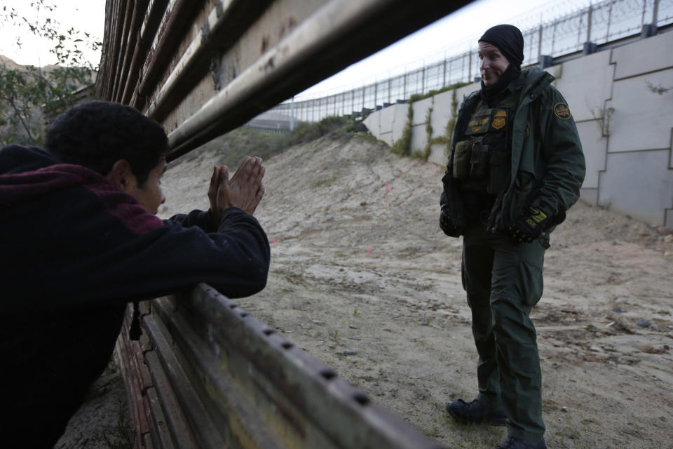 A Honduran migrant pleads with a U.S. Border Patrol agent to let him cross into the U.S., as he peeks through a barrier in Tijuana, Mexico, on Saturday, Dec. 15, 2018. The officer did not respond, and the Honduran did not know the agent would not prevent him from crossing. The man returned to the group of people he was with. (AP Photo/Moises Castillo)