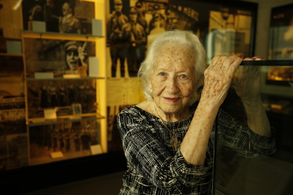 A woman poses with her hands atop a glass display case. Behind her, historical images and artifacts are on display.