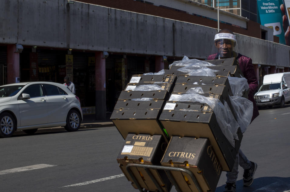 A man wears a face mask to protect against coronavirus, as he pushes a trolley boxes of citrus fruit nearby a taxi rank in downtown Johannesburg, South Africa, Monday, May 11, 2020. (AP Photo/Themba Hadebe)