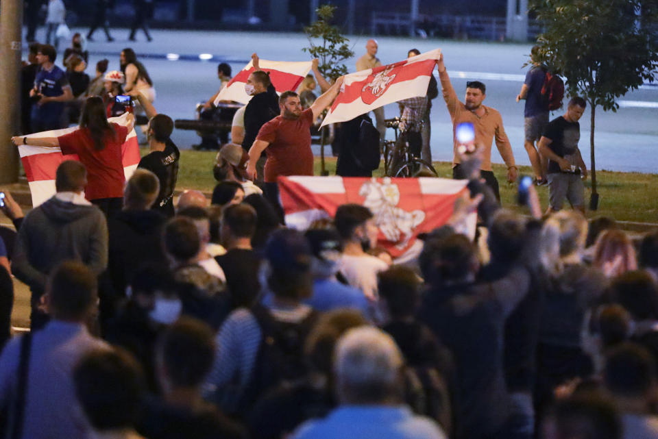 People carry old Belarusian national flags during a mass protest following presidential elections in Minsk, Belarus, Monday, Aug. 10, 2020. Thousands of people have protested in Belarus for a second straight night after official results from weekend elections gave an overwhelming victory to authoritarian President Alexander Lukashenko, extending his 26-year rule. A heavy police contingent blocked central squares and avenues, moving quickly to disperse protesters and detained dozens. (AP Photo/Sergei Grits)