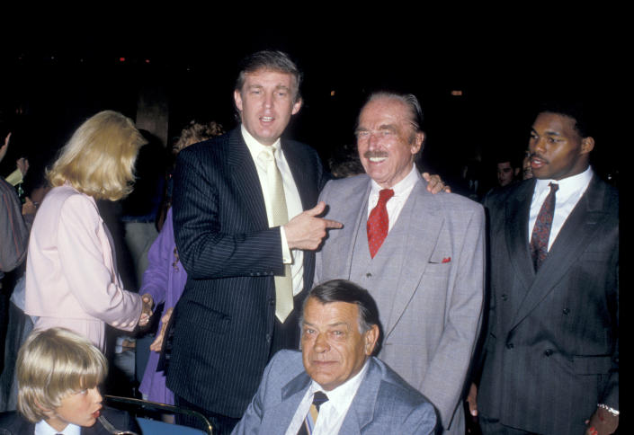 Donald Trump Jr. puts his arm around his father, Fred, flanked by Herschel Walker, with the young Donald Trump Jr., with blond hair, at the bottom of the frame next to an unidentified older man.
