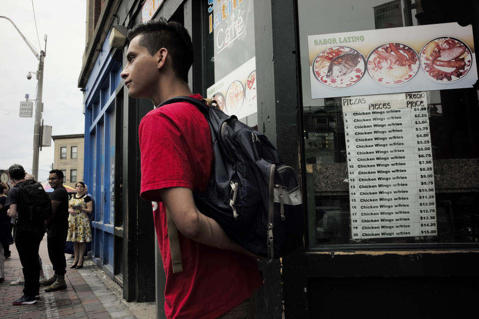 In this Sunday, June 30, 2019 photo people prepare to board a bus outside a Latin-style cafe, right, in Chelsea, Mass. A recent study by the Pew Research Center shows the number of Central Americans in the United States increased over the last decade. Chelsea has exemplified that trend with a population that is more than 60 percent Latino. (AP Photo/Steven Senne)