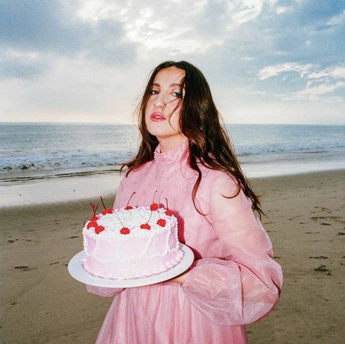 Photo of singer Caity Krone in a pink dress, holding a cake at the beach