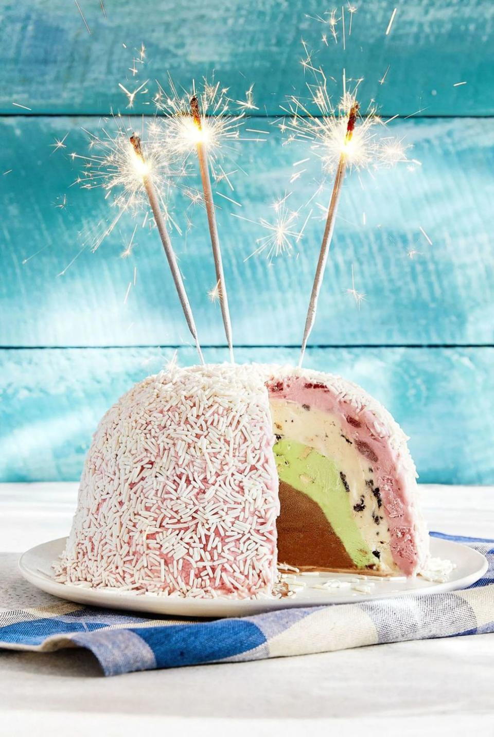 blue bell ice cream bombe with four layers of different ice cream and the whole thing covered in white sprinkles and topped with two sparklers