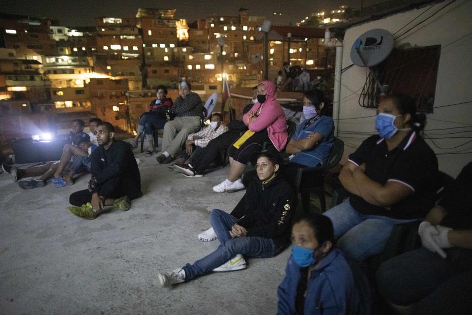 People watch the film Aladdin projected on a screen set up on the roof of a home in the Petare neighborhood of Caracas, Venezuela, late Monday, June 1, 2020. A neighborhood group called The Download Zone set up the movie as a free entertainment option for families cooped up since mid-March under the COVID-19 quarantine. (AP Photo/Ariana Cubillos)