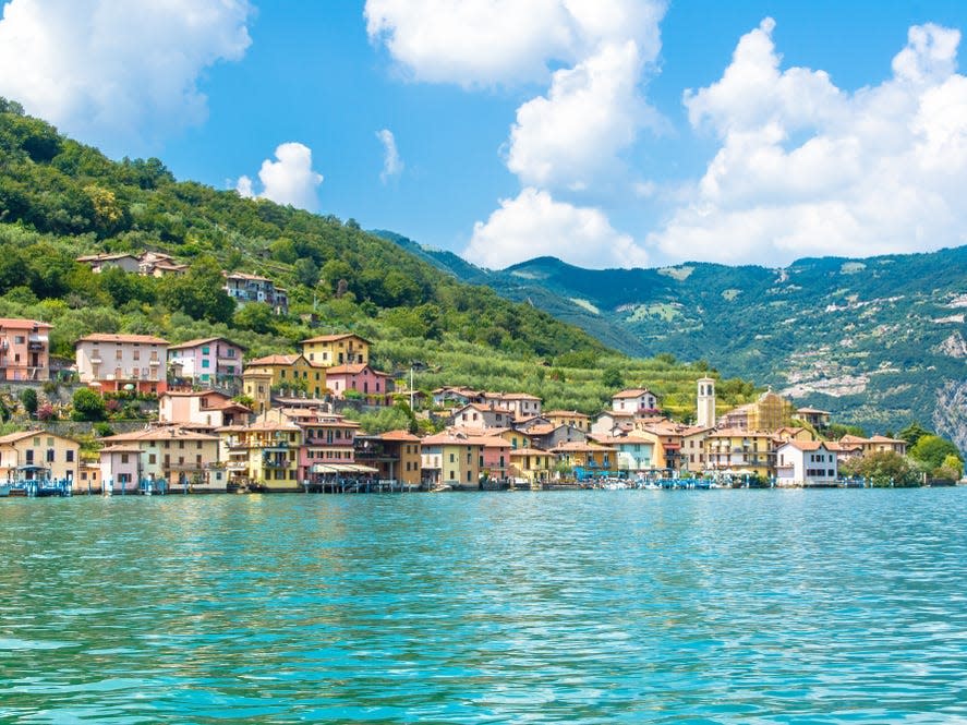 Colorful houses nestled in a greenery-covered mountain next to clear blue waters.