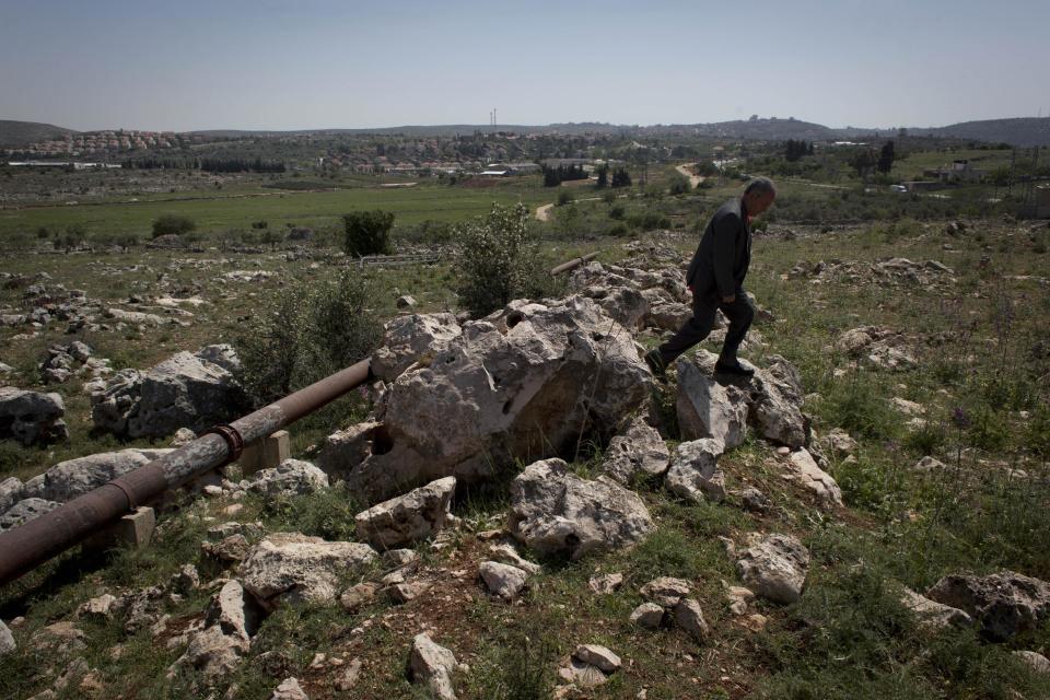 In this April 17, 2014 photo, Abdel Rahman Saleh, the mayor of the Palestinian village of Silwad, inspects his village's land dedicated by the Israeli settlement of Ofra, seen in the background, for an illegal wastewater treatment plant, north of the West Bank city of Ramallah. (AP Photo/Nasser Nasser)