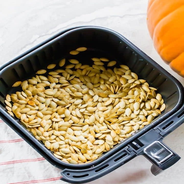 Pumpkin seeds in the basket of an air fryer.