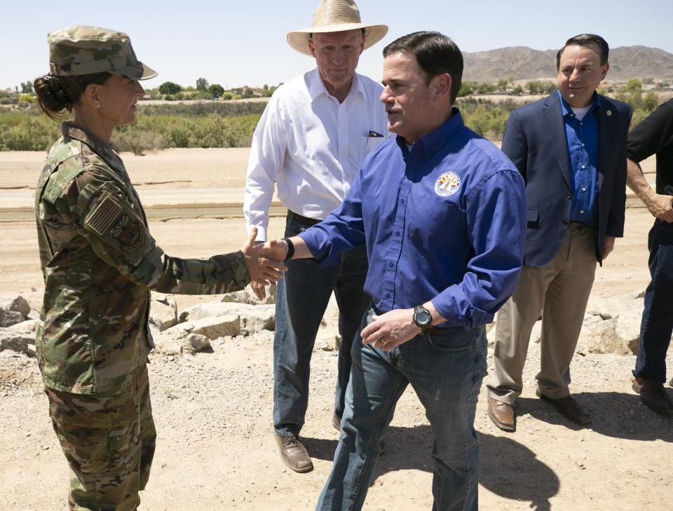 Arizona Governor Doug Ducey shakes hands with Arizona Adjutant General and Director of the Arizona Department of Emergency and Military Affairs Brigadier General Kerry L. Muehlenbeck on the U.S. and Mexico border outside of Yuma on April 21, 2021. Ducey toured the border and spoke during a press conference a day after issuing a Declaration of Emergency and deploying the Arizona National Guard to the border. Arizona Speaker of the House Rusty Bowers, center background, and Yuma Mayor Doug Nicholls, background right, look on.