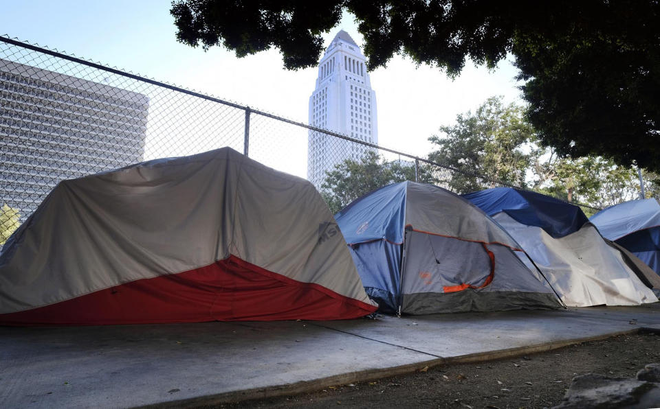 FILE - This Monday, July 1, 2019 file photo shows Los Angeles City Hall behind a homeless tent encampment along a street in downtown Los Angeles. Los Angeles Mayor Eric Garcetti says he hopes President Donald Trump will work with the city to end homelessness as the president visits California for a series of fundraisers. Garcetti says the federal government could aid Los Angeles with surplus property or money to create additional shelters. Garcetti says he has not been invited to meet with the president. (AP Photo/Richard Vogel, File)