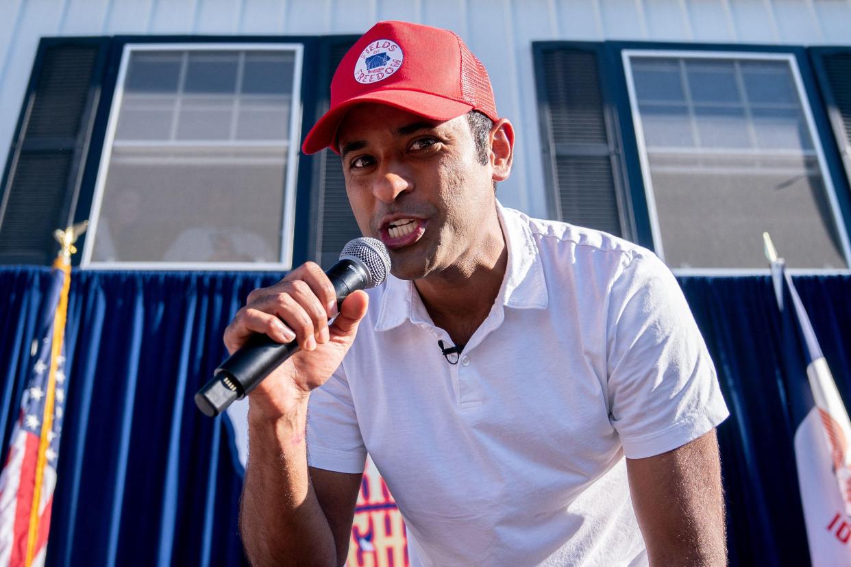 Vivek Ramaswamy, wearing a white polo and a red "Fields of Freedom" cap, raps into a microphone.