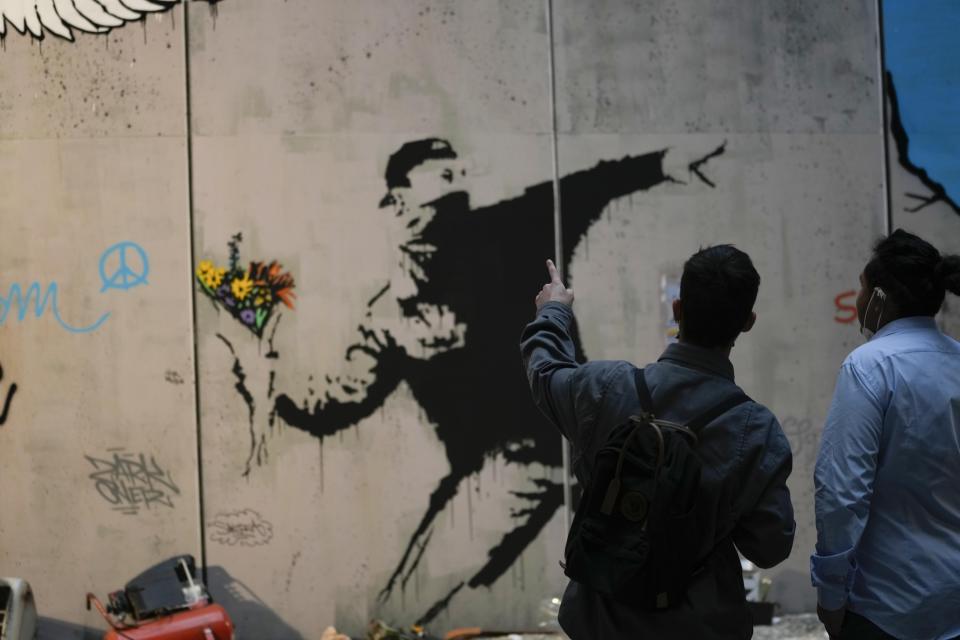 Visitors walk past "Flower Thrower", a reproduction of a mural by British artist Banksy, during the unveiling of the "The World of Banksy, The Immersive Experience" exhibition, in Milan, Italy, Thursday, Dec. 2, 2021. An exhibition of 130 works by British street artist Banksy opens Friday in a gallery space inside Milan's Central train Station. The exhibition unveiled on Thursday includes 30 never before seen works by Bansky and highlights pieces by young unknown artists from all over Europe. (AP Photo/Luca Bruno)