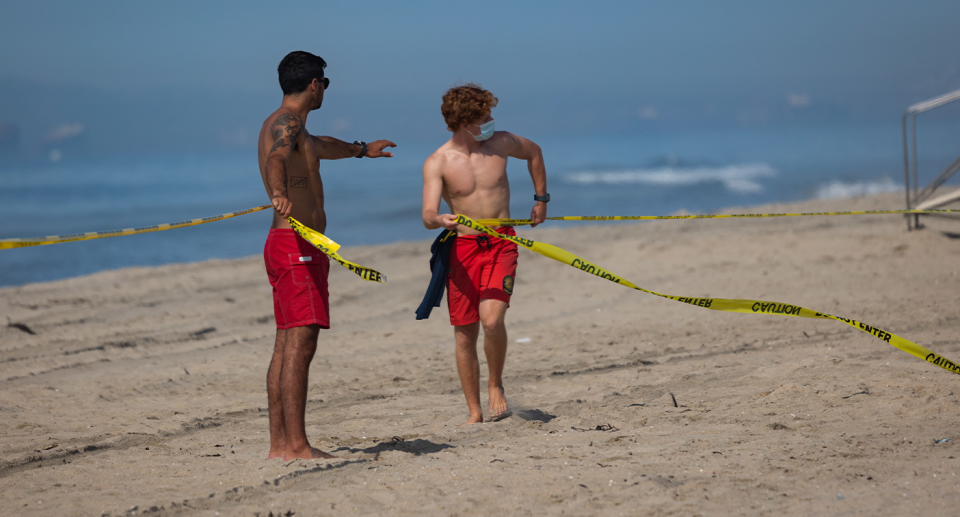 Two lifeguards roping off Huntington Beach using police tape. 