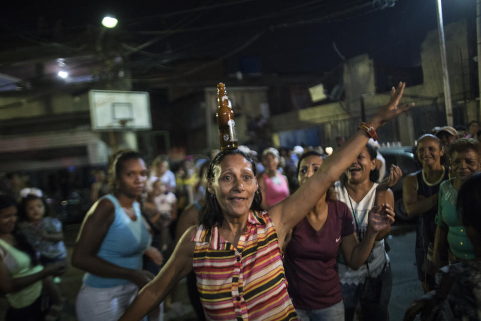 In this Sunday, May 19, 2019 photo, a woman jokes around with a full bottle of beer on her head as she celebrates winning the dancing contest at a Mother's Day block party in Caracas, Venezuela. Although Mother's Day was officially celebrated the previous weekend, people in the Petare area organized the neighborhood party to celebrate the mothers of their community. (AP Photo/Rodrigo Abd)