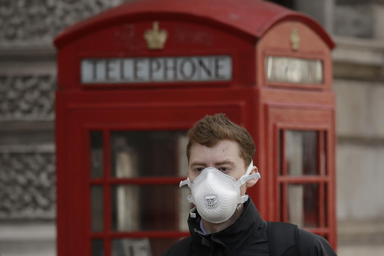 A man wearing a face mask walks past a traditional British red phone box just off Parliament Square in central London, Wednesday, March 11, 2020. A British government minister Nadine Dorries, who is a junior Heath minster has tested positive for the coronavirus and is self isolating. For most people, the new coronavirus causes only mild or moderate symptoms, such as fever and cough. For some, especially older adults and people with existing health problems, it can cause more severe illness, including pneumonia. (AP Photo/Matt Dunham)