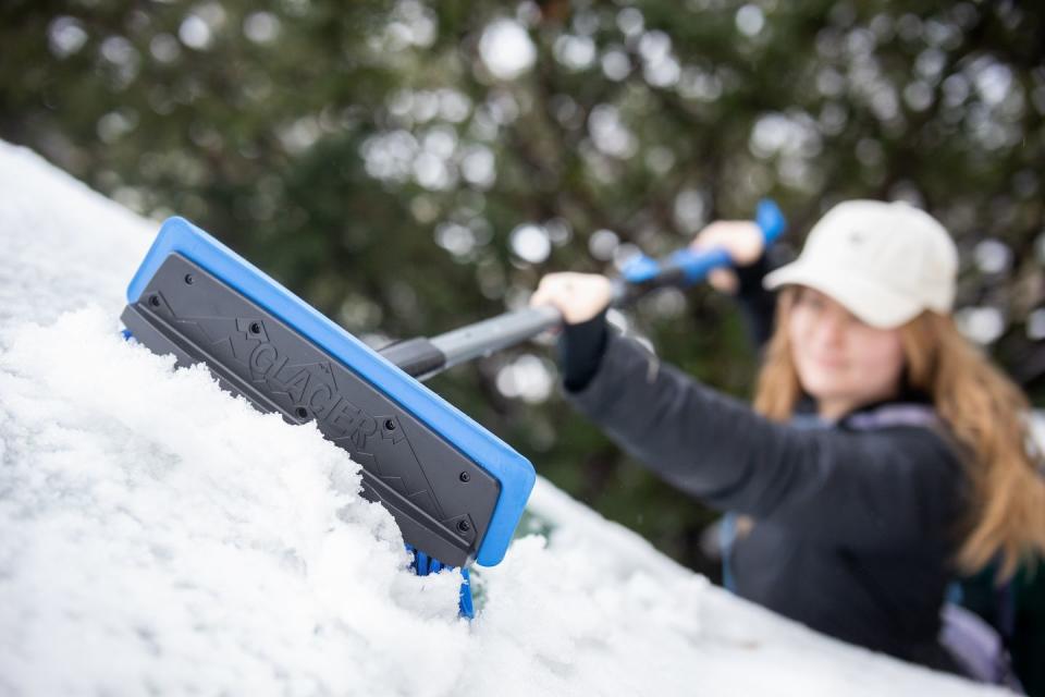 person using brush to remove snow on car