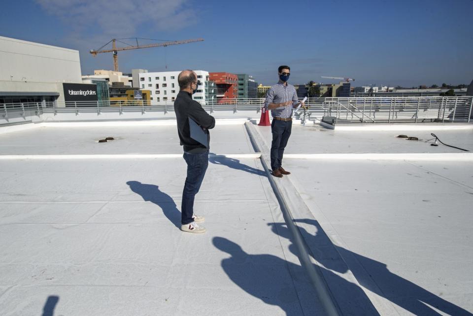 Two people on the roof of a building on a sunny day with cranes in the background