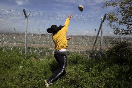 A protesting migrant throws stones at Macedonian police during clashes next to a border fence at a makeshift camp for refugees and migrants at the Greek-Macedonian border near the village of Idomeni, Greece, April 10, 2016. REUTERS/Alexandros Avramidis