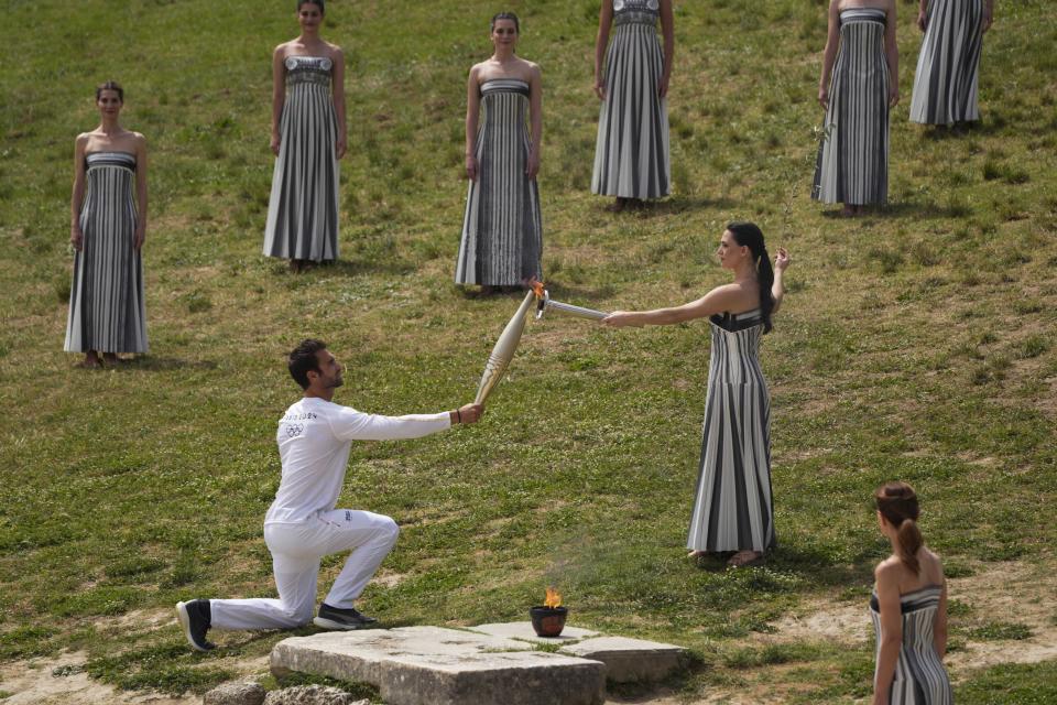 Actress Mary Mina, playing high priestess, gives the flame to the first torch bearer, Greek olympic gold medalist Stefanos Douskos during the official ceremony of the flame lighting for the Paris Olympics, at the Ancient Olympia site, Greece, Tuesday, April 16, 2024. The flame will be carried through Greece for 11 days before being handed over to Paris organizers on April 26. (AP Photo/Petros Giannakouris)