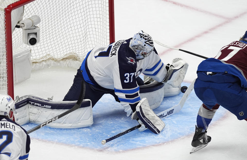 Winnipeg Jets goaltender Connor Hellebuyck, left, stops a shot from Colorado Avalanche center Casey Mittelstadt during the first period of Game 3 of an NHL hockey Stanley Cup first-round playoff series Friday, April 26, 2024, in Denver. (AP Photo/David Zalubowski)