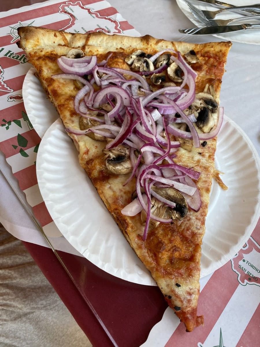 Onion and mushroom pizza, Benny Tudino’s, Hoboken, New Jersey, on two paper plates, on a maroon table with table-mats, utensils on the top