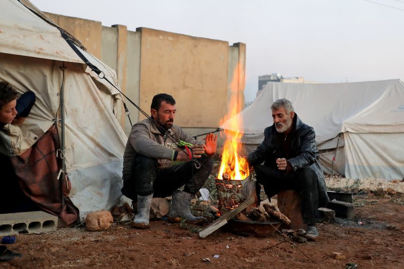 Internally displaced Syrians warm themselves around a fire at a camp in the Northern Aleppo countryside