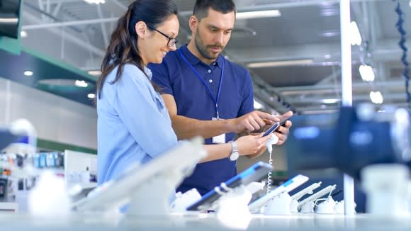 A store employee helps a customer with mobile phones.