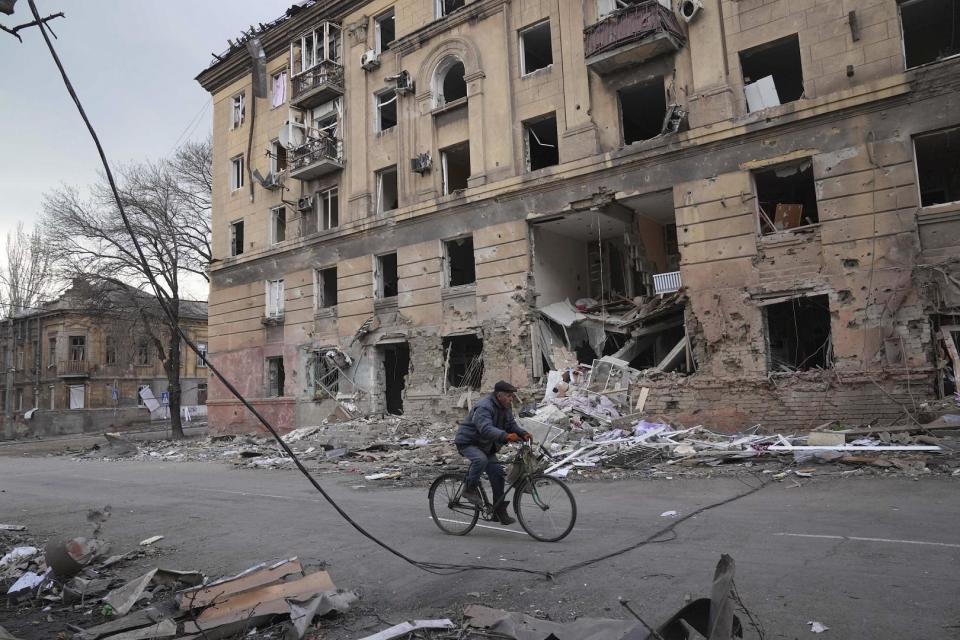 Ein Mann fährt mit dem Fahrrad vor einem durch Granatenbeschuss beschädigten Wohnhaus in Mariupol, Ukraine. 9. März 2022