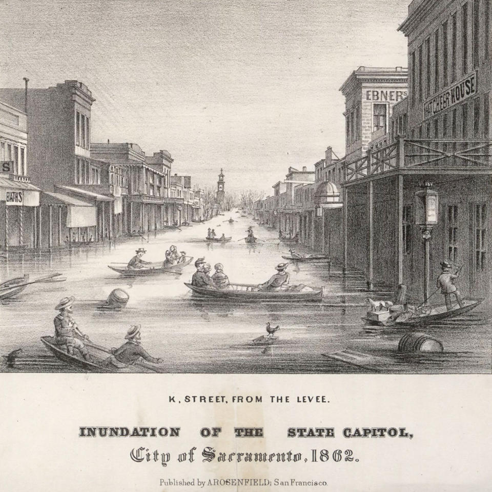 A dozen flat boats, some propelled by poles, each carrying up to four passengers and in some cases, small dogs, float on a city street in an engraving titled: K. Street, From the Levee. Inundation of the State Capitol, City of Sacrament, 1862, Published by A. Rosenfield, San Francisco.