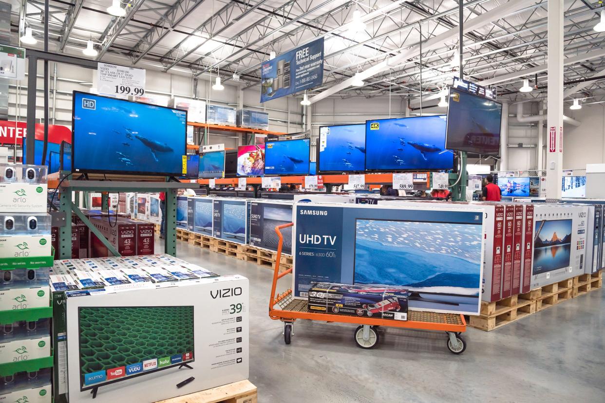 Row of big screen, smart TVs displayed on shelves and on flatbed cart at Costco Wholesale.