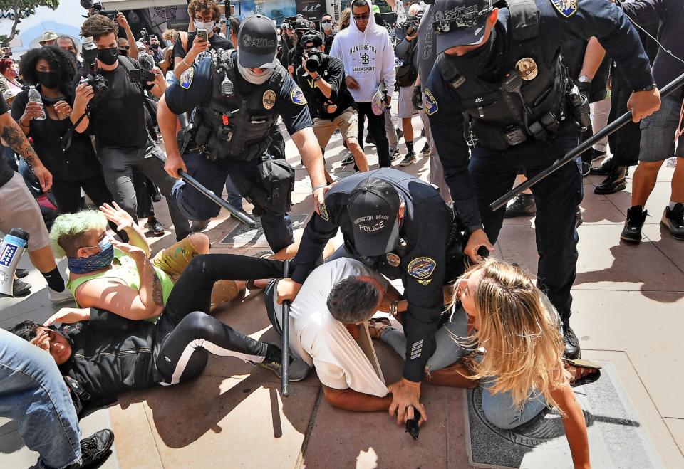 A crowd watches police officers break up a scuffle among several people on the concrete.