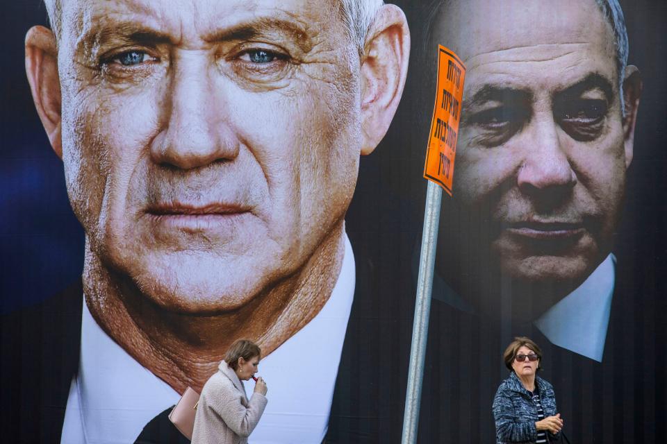People walk by an election campaign billboard for the Blue and White party, the opposition party led by Benny Gantz, left, in Ramat Gan, Israel, on Feb. 20, 2020. Prime Minister Benjamin Netanyahu of the Likud party is pictured at right