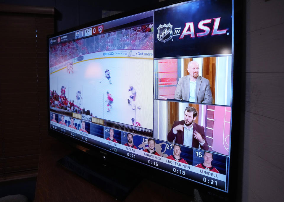 Jason Altmann, top right, and Noah Blankenship deliver play-by-play and commentary for the hearing impaired during the Stanley Cup hockey final, seen on a television, Monday, June 10, 2024 in Genoa Township, Mich. Bob Madden is deaf and he was enjoying the view with access to the commentary delivered in American Sign Language for the first time during a sporting event. The NHL became the first major sports league to offer play by play and analysis in ASL during a live broadcast. (AP Photo/Carlos Osorio)