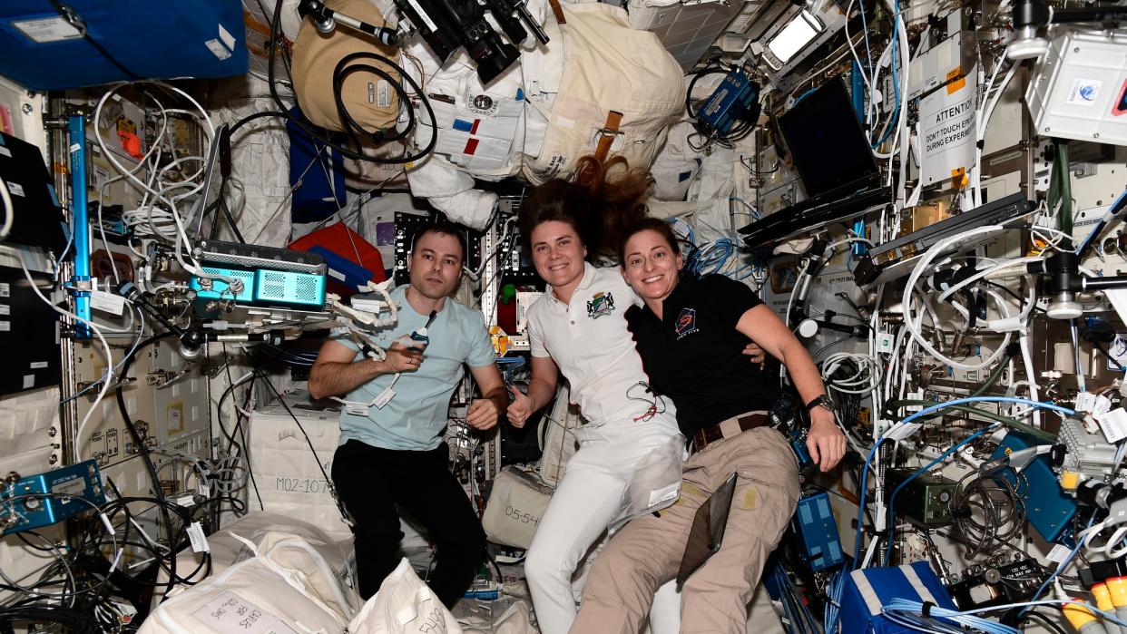  three astronauts in the middle of a module absolutely stuffed with equipment, spacesuits and electronics 