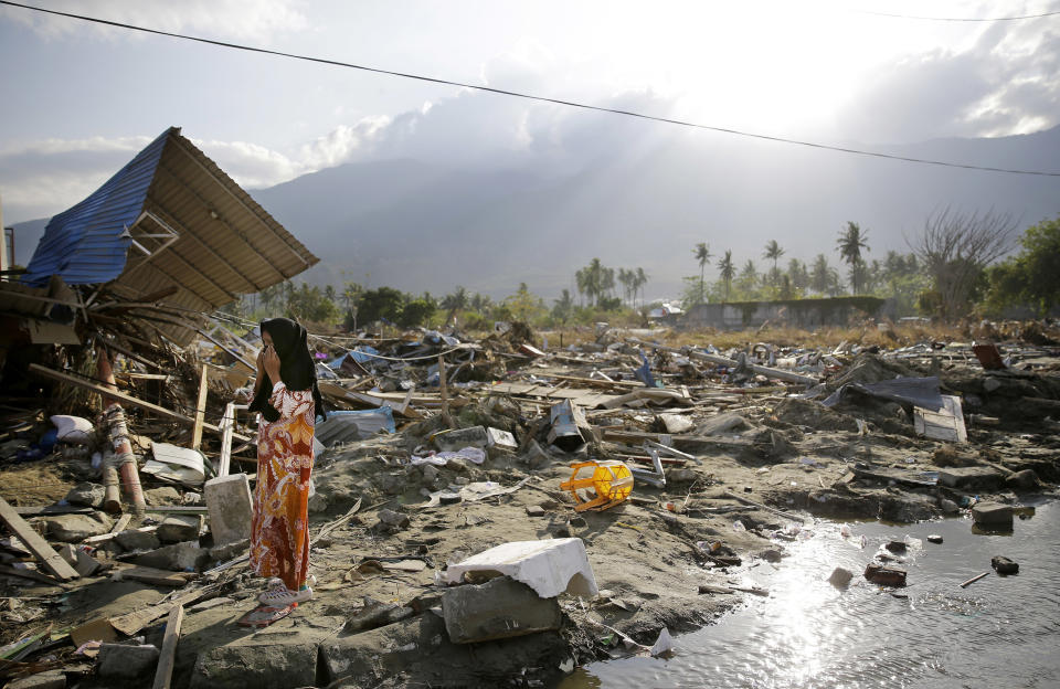 In this Oct. 4, 2018, file photo, a woman walks past toppled structures along a busy road in the earthquake and tsunami-damaged Palu, Central Sulawesi, Indonesia. (AP Photo/Aaron Favila, File)