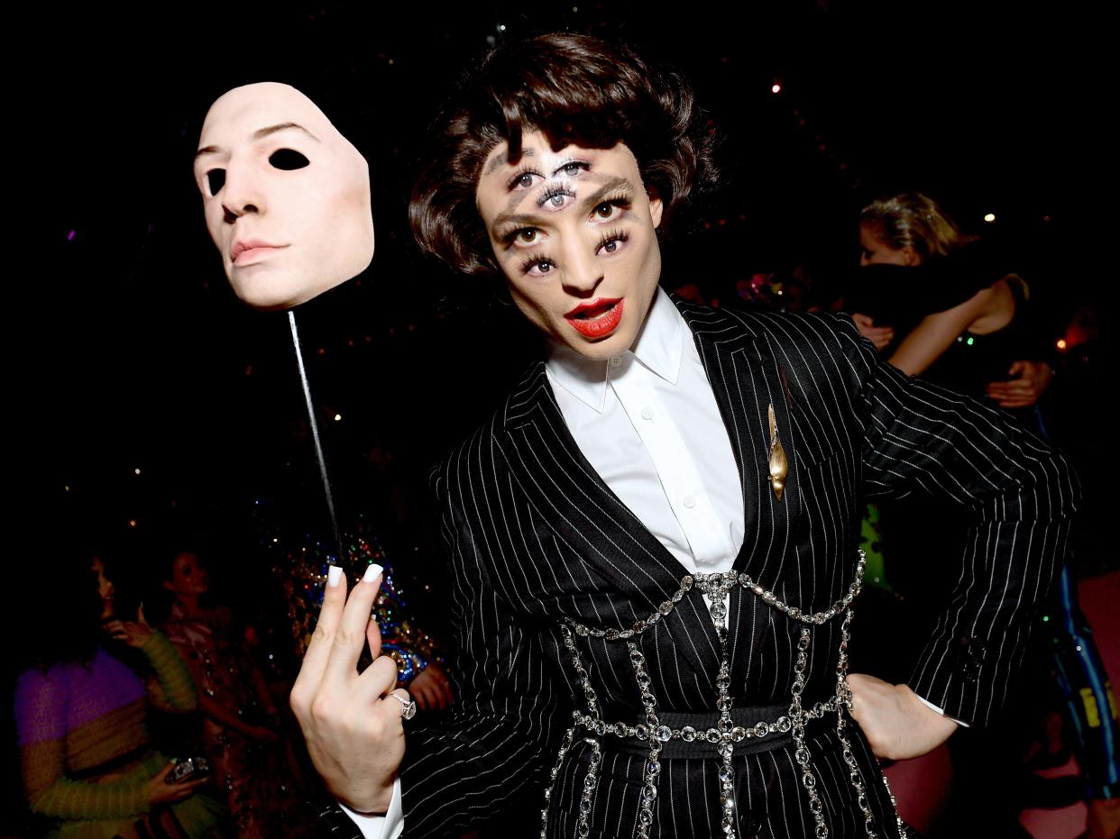 Ezra Miller holding a mask with multiple sets of eyes on their face.