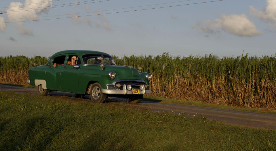 In this Sept. 8, 2012 photo, people drive a classic American car past a sugar cane field in Camaguey, Cuba. Just two years ago, Cuba's sugar industry was on its knees after the worst harvest in more than a century. Now Cuba's signature industry is showing signs of life. With world market prices rebounding, sugar is suddenly more profitable, and a reorganization of the sector could offer a blueprint for how to lift up the rest of the island's economy. (AP Photo/Franklin Reyes)