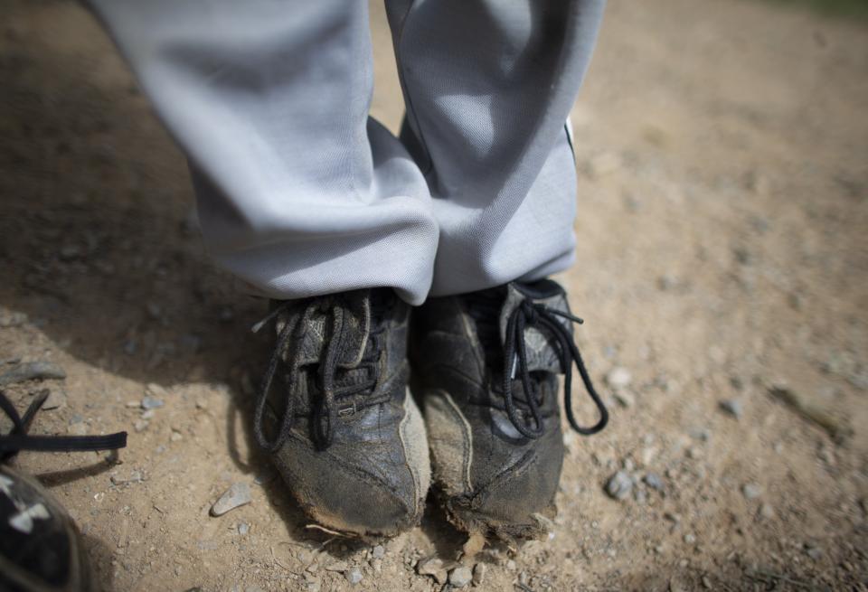 In this Aug. 12, 2019 photo, a young baseball player stands on the field in a pair of worn cleats during a practice at Las Brisas de Petare Sports Center, in Caracas, Venezuela. The South American country was an incubator of Major League Baseball stars such as Miguel Cabrera and Felix Hernandez, but now the troubled country is struggling to showcase emerging talent. (AP Photo/Ariana Cubillos)