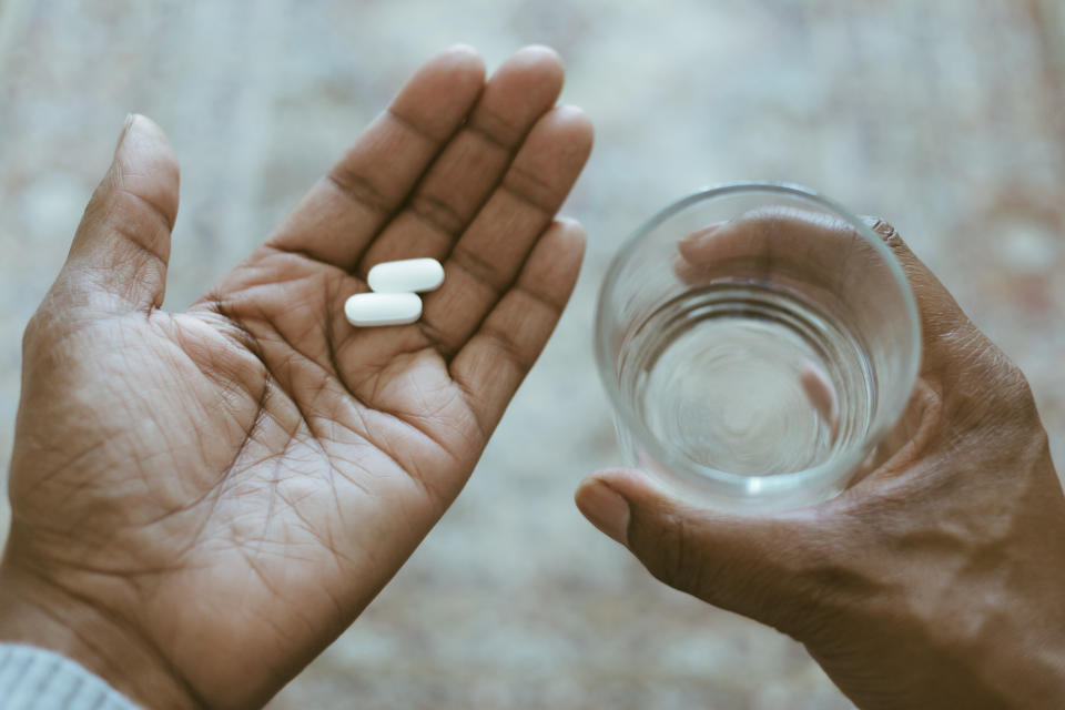 A man holds pills and a glass of water.