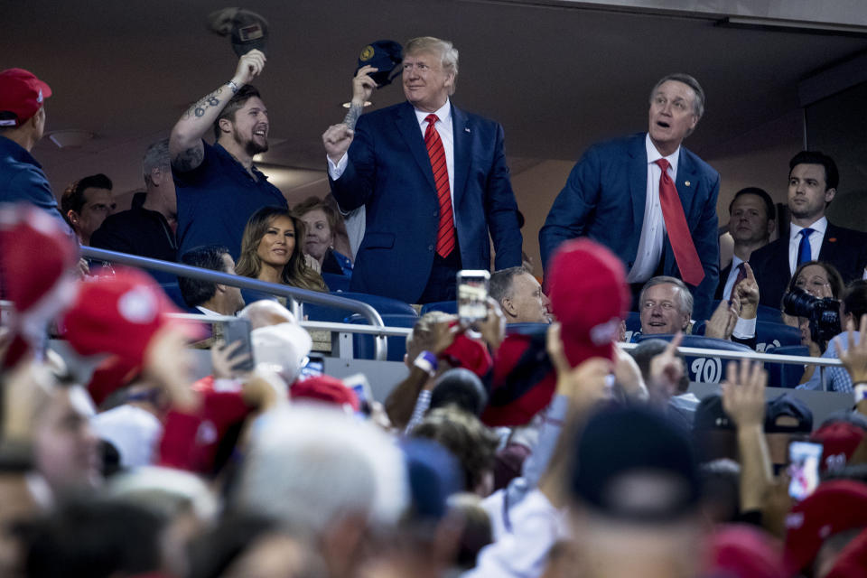 President Donald Trump, center, accompanied by Sen. David Perdue, R-Ga., right, and a member of the military, left, stands as members of the military are recognized during Game 5 of a baseball World Series between the Houston Astros and the Washington Nationals at Nationals Park in Washington, Sunday, Oct. 27, 2019. (AP Photo/Andrew Harnik)