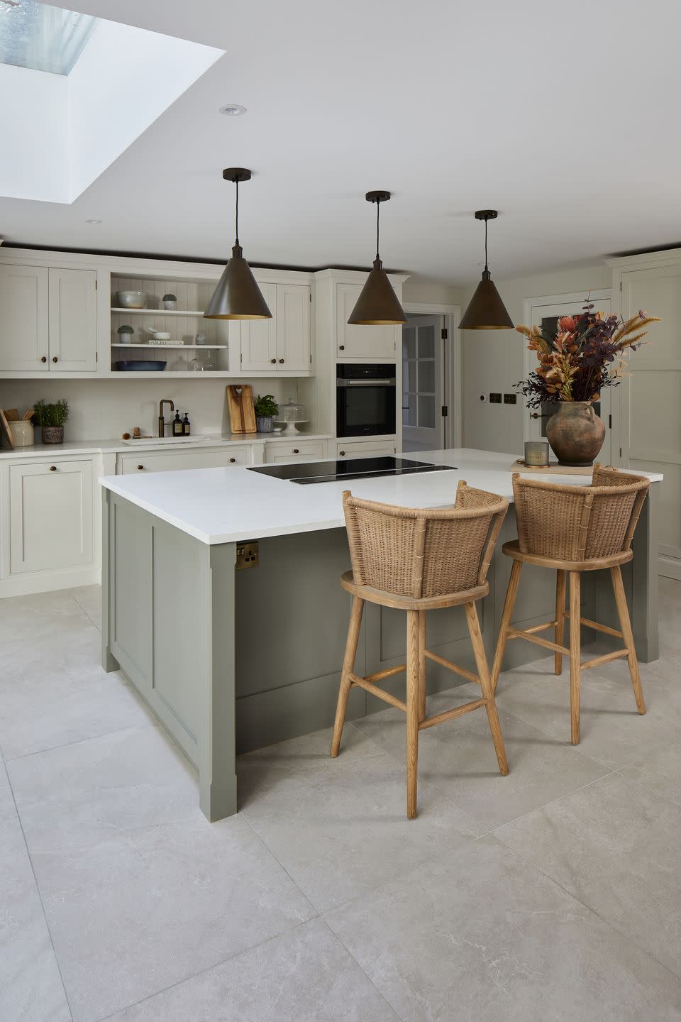 a grey kitchen with pale grey porcelain floor tiles, a breakfast bar and rattan bar stools