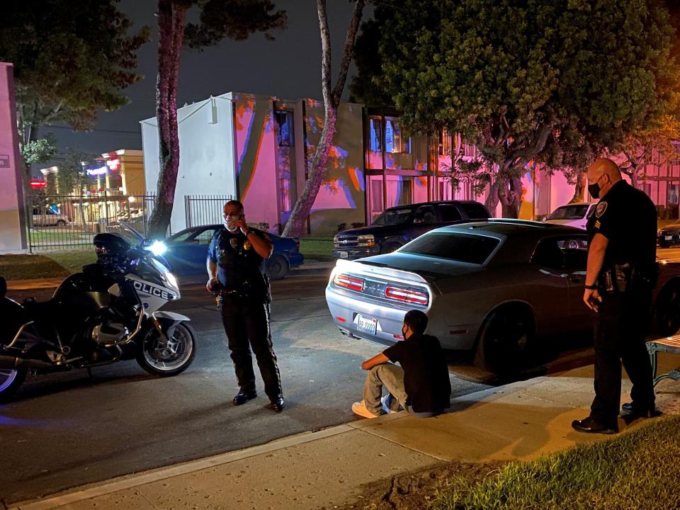 A driver sits on the sidewalk after being pulled over during street-racing enforcement operation Thursday, Aug. 20, 2020, in Oxnard, Calif.