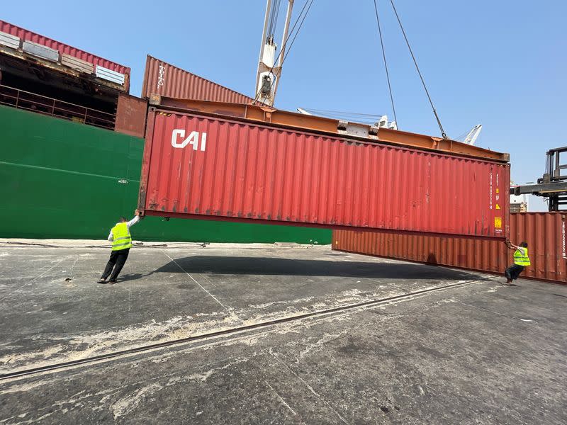 Workers help a crane operator unloading a container from a commercial ship in the Houthi-held Red Sea port of Hodeidah