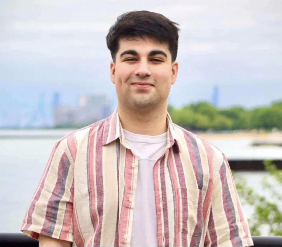 A young man with dark brown hair smiles in a portrait shot in front of the Chicago skyline. HE's wearing a white T-shirt under a red and orange striped button down. (Courtesy of Moshi family / WMAQ)