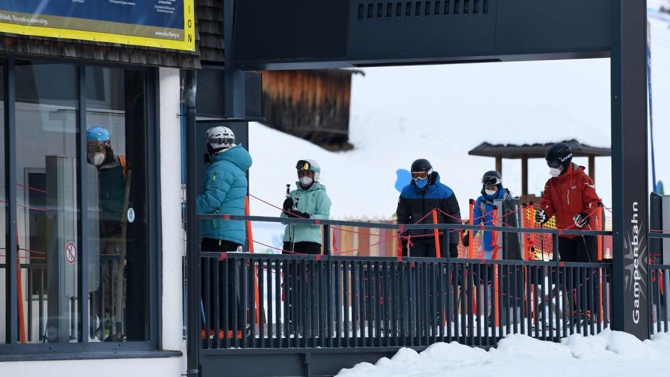 Wintersportler stehen in Tirol mit Mund-Nasen-Schutz an einem Skilift an.