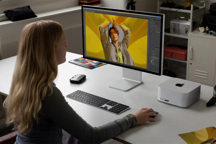 A woman sits at a desk with the M2 Mac Studio on it.