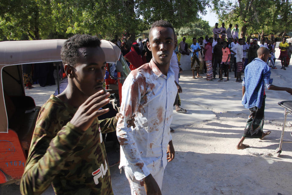 A civilian who was wounded in suicide car bomb attack is helped by a friend at check point in Mogadishu, Somalia, Saturday, Dec, 28, 2019. A police officer says a car bomb has detonated at a security checkpoint during the morning rush hour in Somalia's capital. (AP Photo/Farah Abdi Warsame)