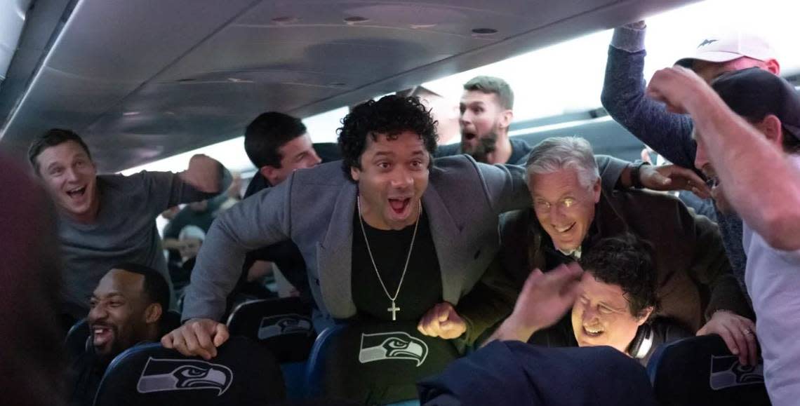 Russell Wilson (center), Pete Carroll (right) and the Seahawks erupt in cheers aboard their chartered jet taking them home from their win at Carolina Sunday, after they learned the Atlanta Falcons beat the San Francisco 49ers. The Niners’ loss put Seattle (11-3) back in first place in the NFC West with two regular-season games remaining.