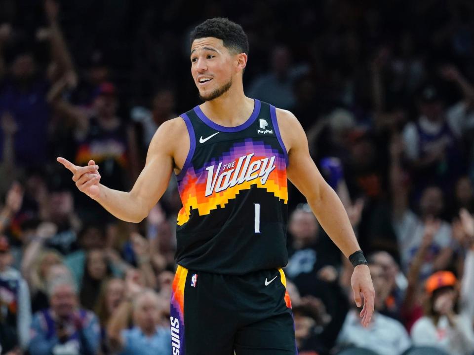Devin Booker smiles and points during a game.